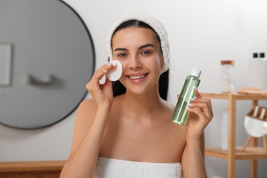 Photo of Young woman using cotton pad with micellar water indoors