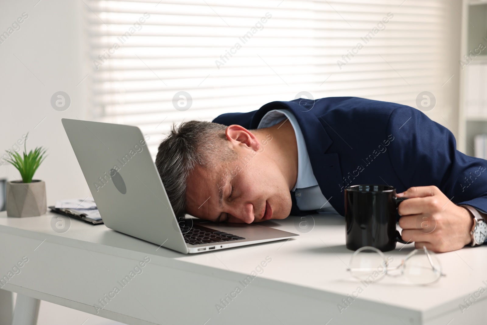 Photo of Man with cup of drink sleeping at table in office