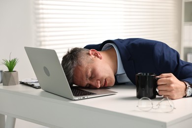 Man with cup of drink sleeping at table in office