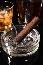 Smoldering cigar, ashtray and whiskey on black mirror surface, closeup