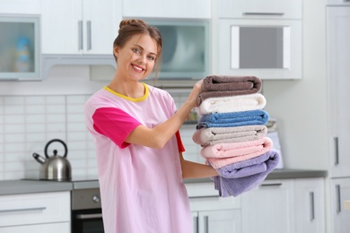 Photo of Happy young woman holding clean laundry in kitchen