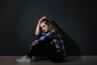 Photo of Depressed young woman sitting on floor in darkness