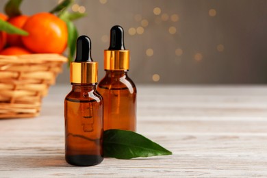 Bottles of tangerine essential oil and green leaf on white wooden table, closeup. Space for text