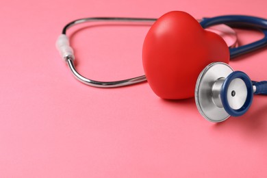 Photo of Stethoscope, red decorative heart and space for text on pink background, closeup. Cardiology concept