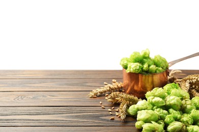 Fresh hop flowers and wheat ears on wooden table against white background, space for text