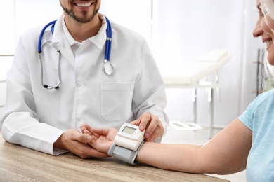 Doctor checking mature woman's pulse with medical device in hospital, closeup