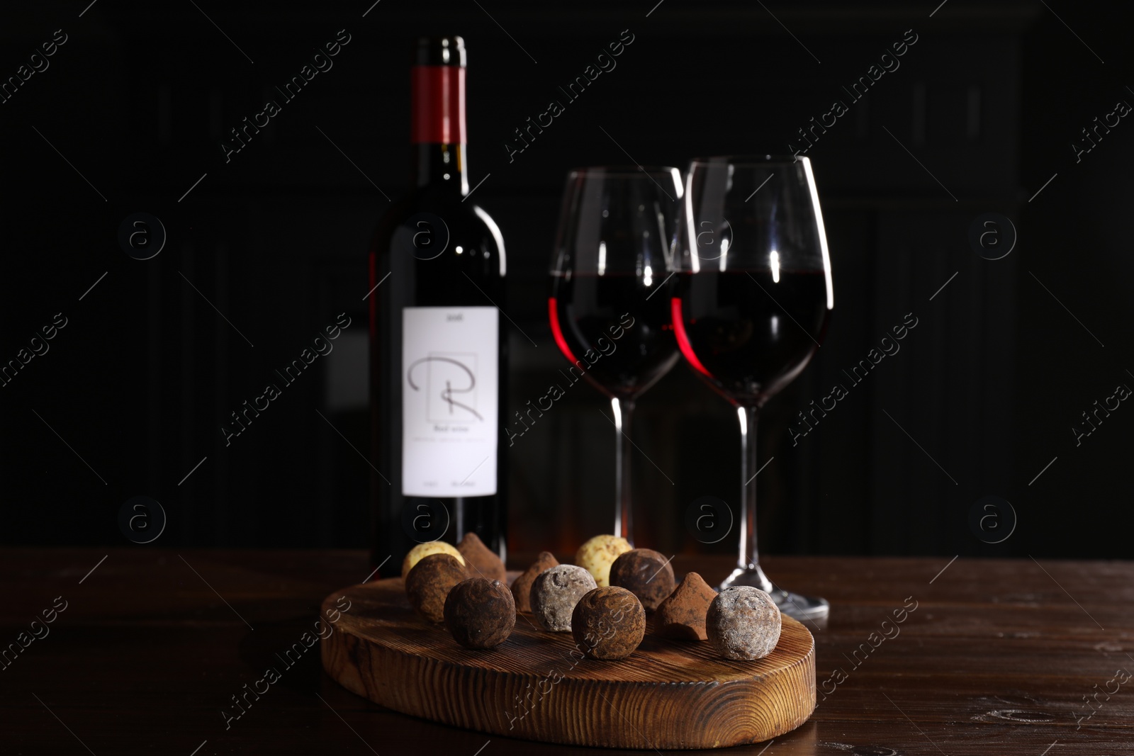 Photo of Red wine and chocolate truffles on wooden table against dark background
