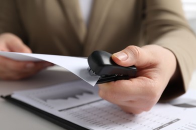 Photo of Woman with papers using stapler at white table, closeup