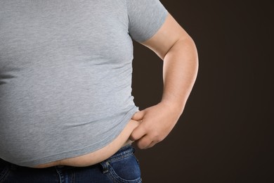 Photo of Overweight man in tight t-shirt on dark brown background, closeup. Space for text.