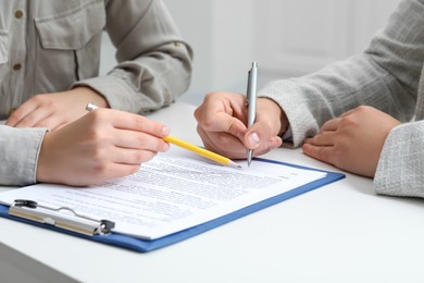 Photo of Woman pointing at document and man signing at white table, closeup