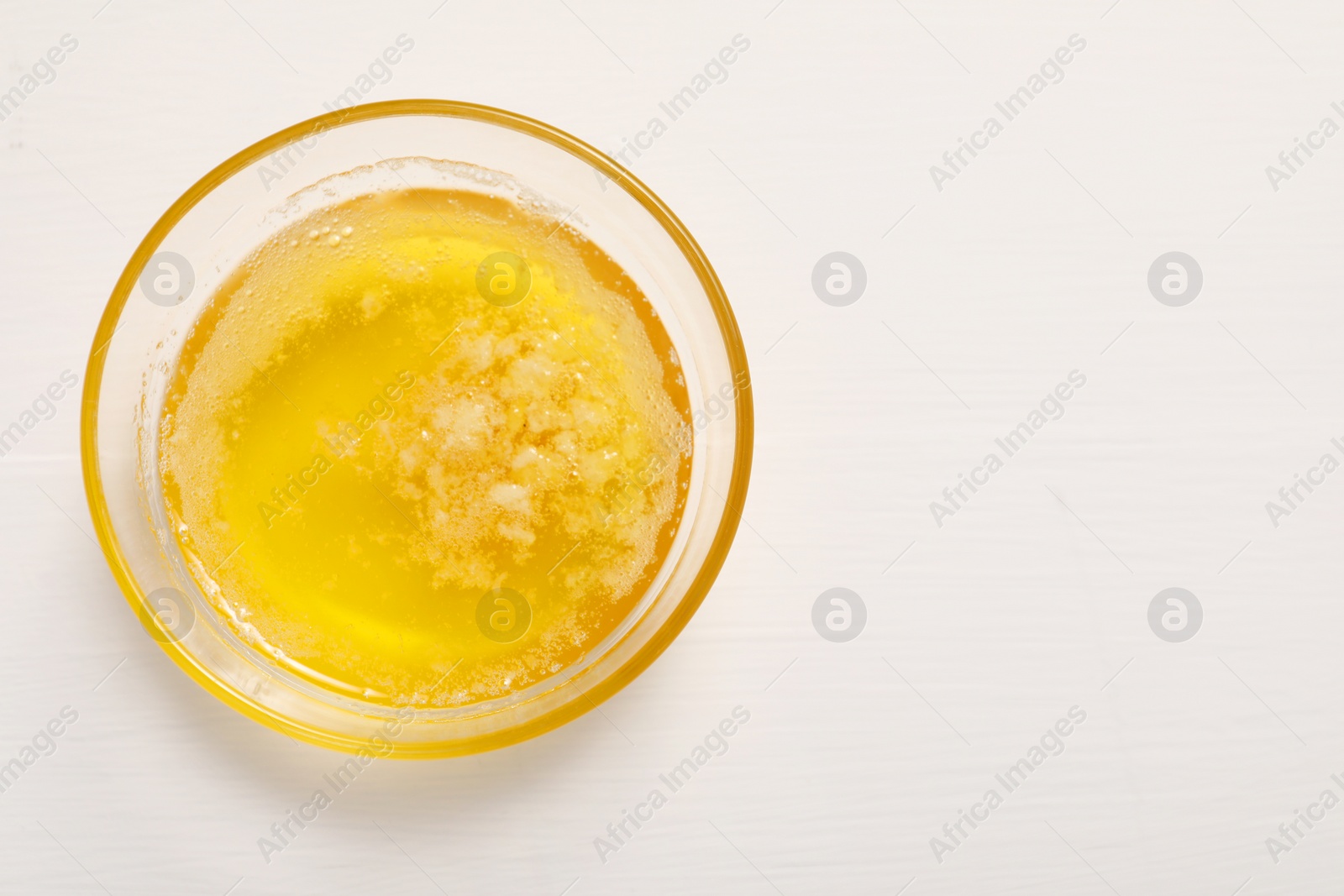 Photo of Melted butter in glass bowl on white wooden table, top view. Space for text