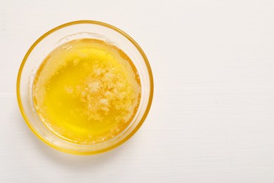 Photo of Melted butter in glass bowl on white wooden table, top view. Space for text