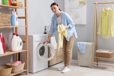 Photo of Beautiful woman with sweatshirt near washing machine in laundry room