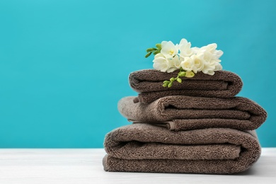 Stack of soft clean towels with beautiful flowers on table against color background. Space for text