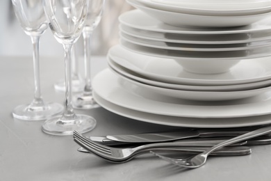 Photo of Stacked plates, cutlery and glasses on light grey table, closeup