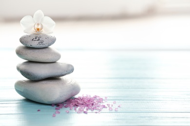 Photo of Spa stones, sea salt and flower on table against blurred background. Space for text