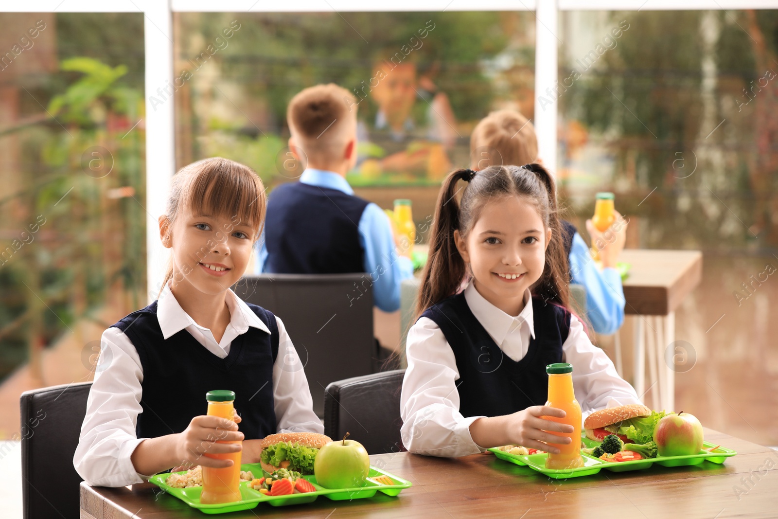 Photo of Happy girls at table with healthy food in school canteen