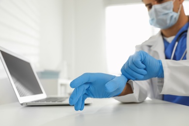 Photo of Doctor putting on medical gloves at table in office, closeup