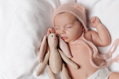 Photo of Cute little baby with toy bunny sleeping on soft bed, top view