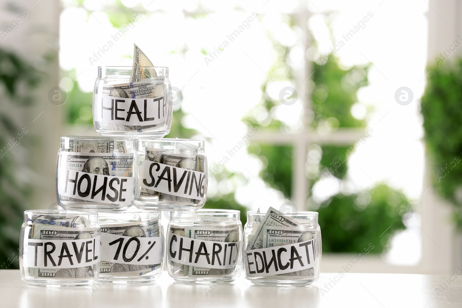 Photo of Glass jars with money for different needs on table against blurred background, space for text