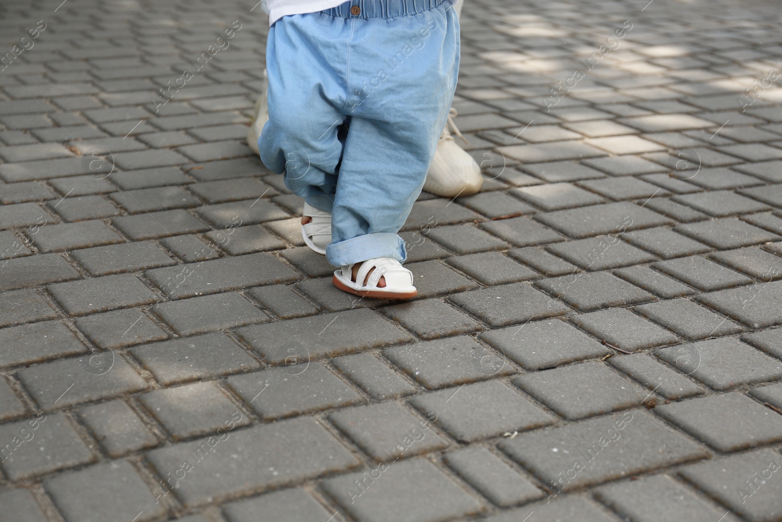 Photo of Mother supporting daughter while she learning to walk outdoors, closeup. Space for text