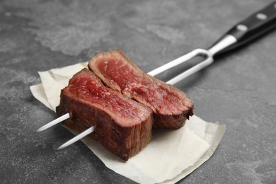 Photo of Carving fork with slices of delicious beef steak on grey table, closeup