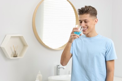 Photo of Young man using mouthwash in bathroom. Oral hygiene