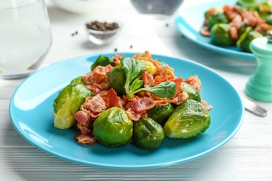 Tasty roasted Brussels sprouts with bacon on white wooden table, closeup