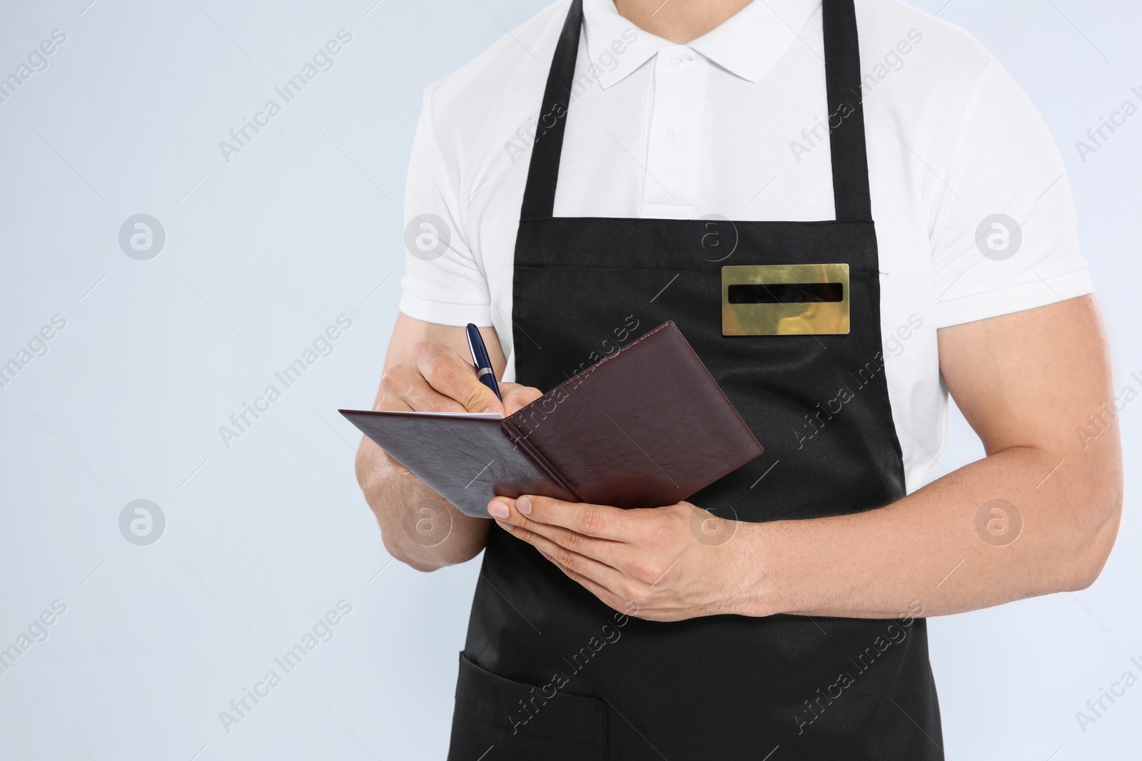 Photo of Young waiter in apron taking order on light background