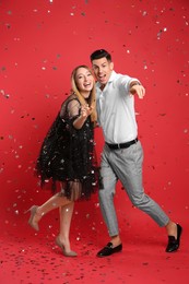 Happy couple and confetti on red background