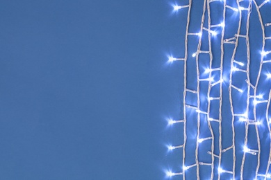 Photo of Christmas lights on blue background, top view. Space for text