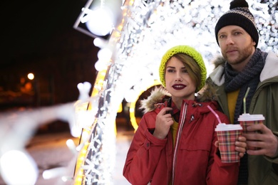 Young couple with cups of mulled wine at winter fair. Space for text