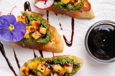 Photo of Delicious bruschettas with pesto sauce,tomatoes, balsamic vinegar and violet flower on white plate, flat lay