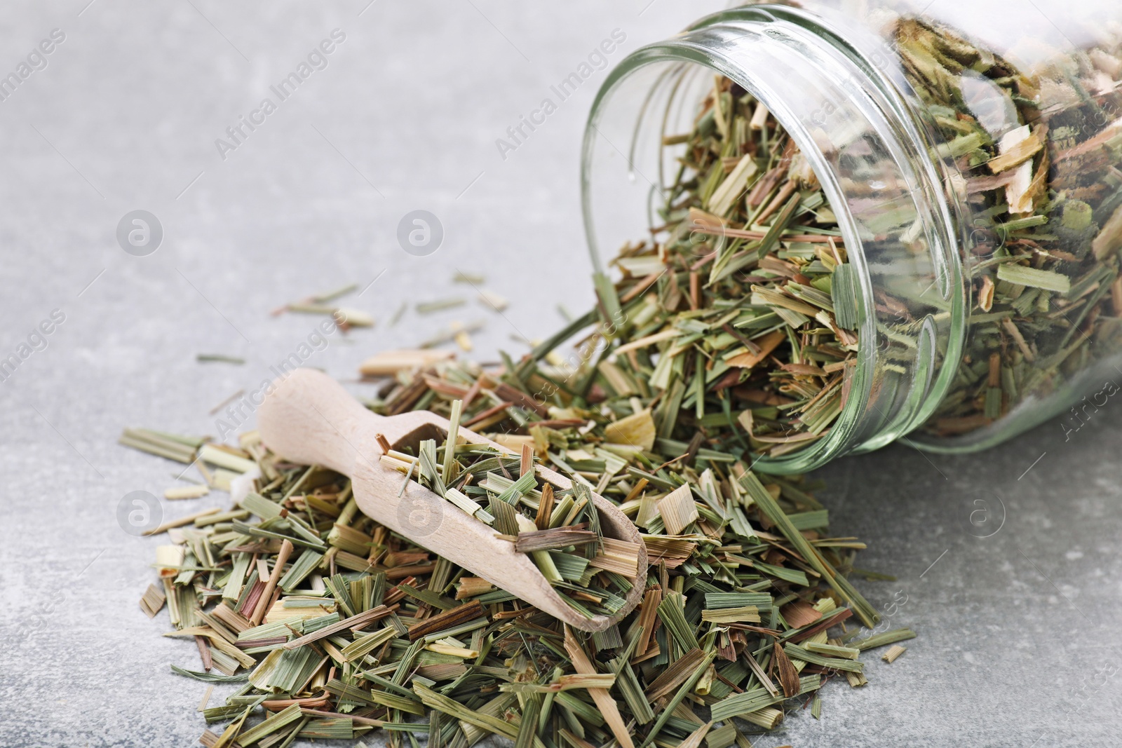 Photo of Jar and scoop with aromatic dried lemongrass on light grey table, closeup