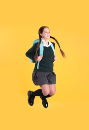Photo of Teenage girl in school uniform with backpack jumping on yellow background