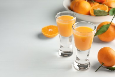 Photo of Tasty tangerine liqueur in shot glasses and fresh fruits on white table. Space for text