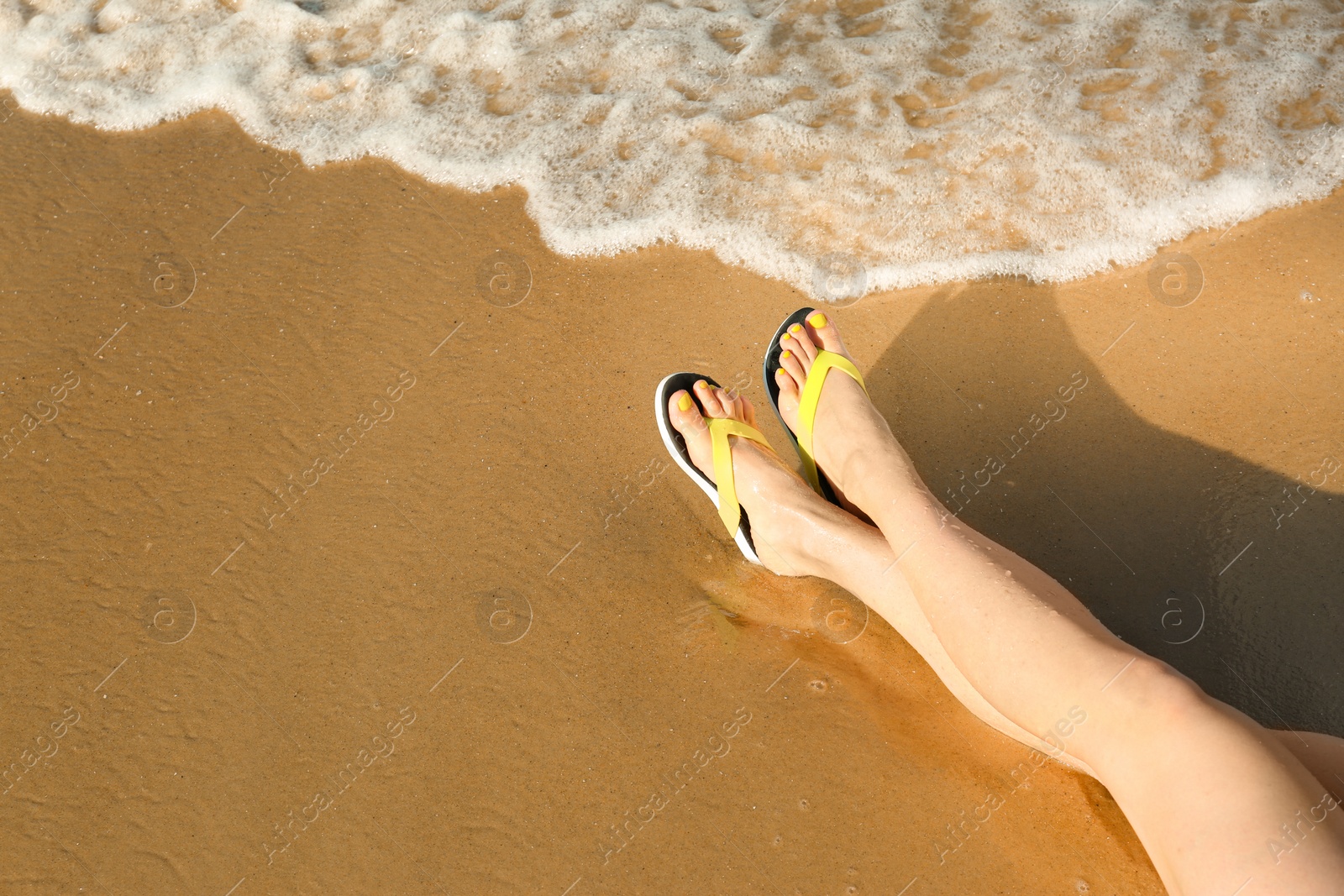 Photo of Closeup of woman with flip flops on sand near sea, space for text. Beach accessories