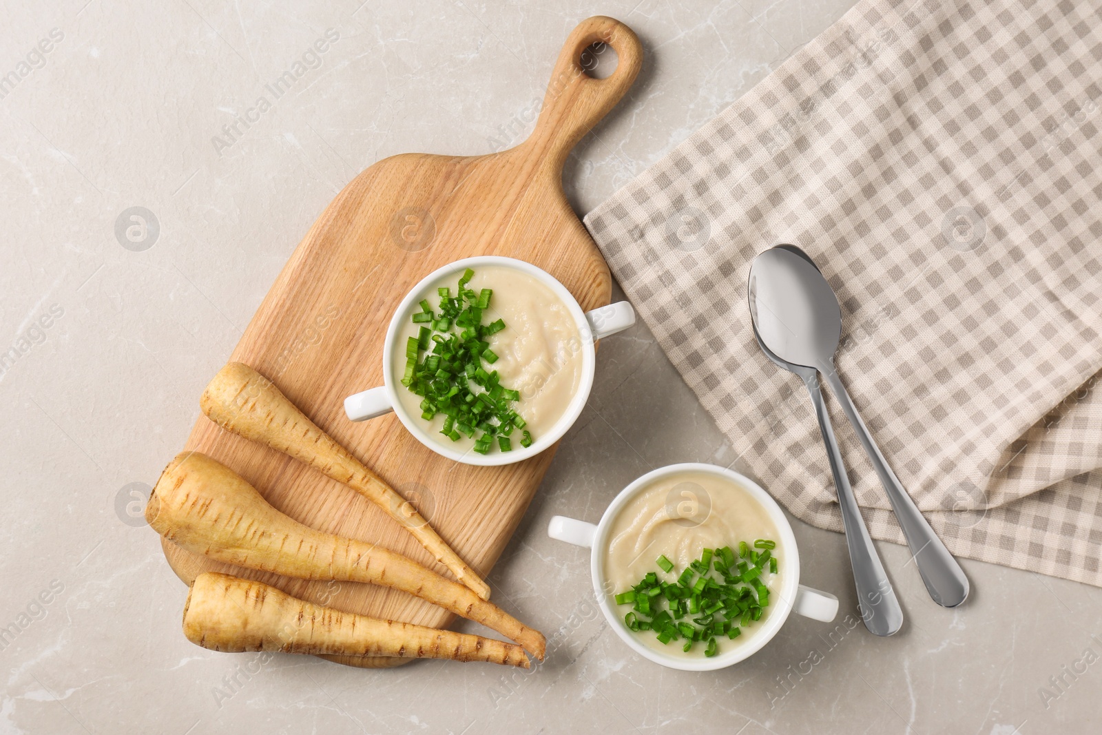 Photo of Bowls with tasty creamy soup of parsnip served on light grey table, flat lay