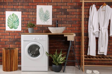 Photo of Washing machine and wooden rack with terry bathrobes indoors. Laundry room interior design