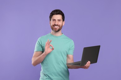 Photo of Happy man with laptop showing ok gesture on purple background