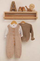 Wooden shelf with baby clothes and toys on white wall