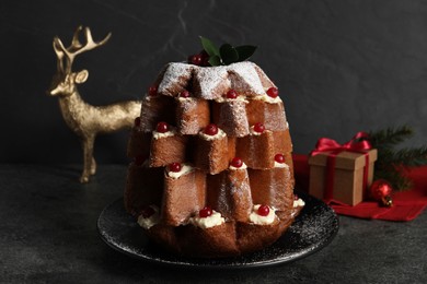 Delicious Pandoro Christmas tree cake with powdered sugar and berries near festive decor on black table
