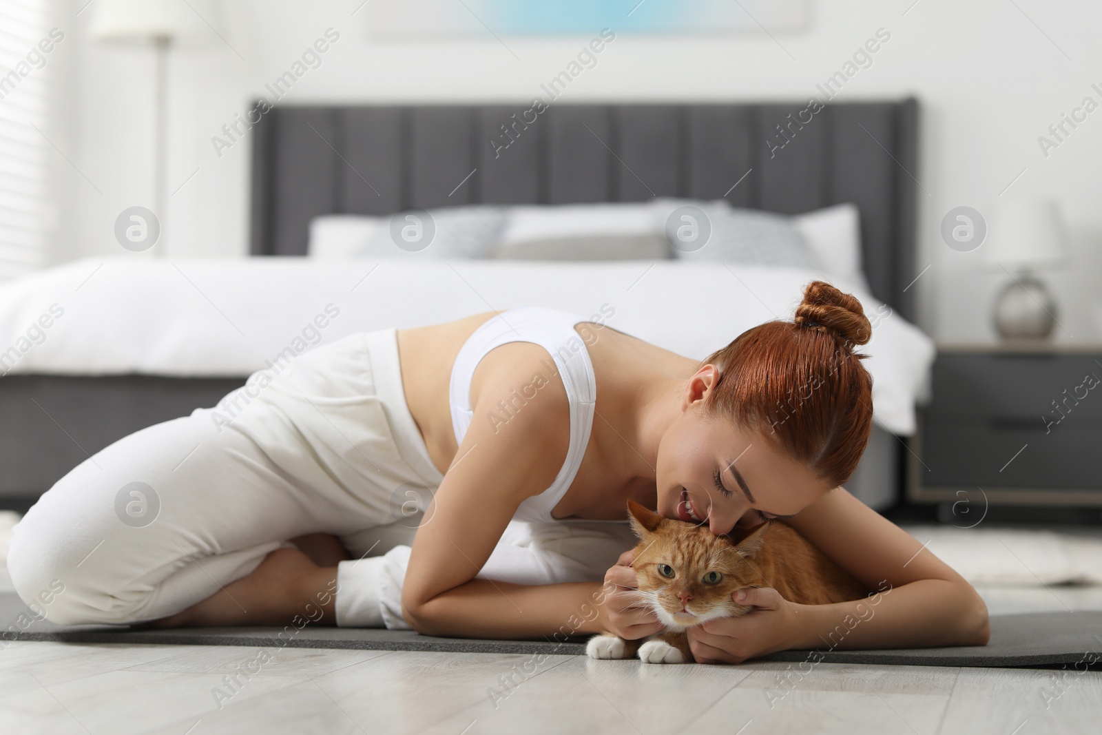 Photo of Beautiful woman petting cute red cat on mat at home. Practicing yoga