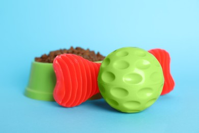 Pet toys and bowl of food on light blue background