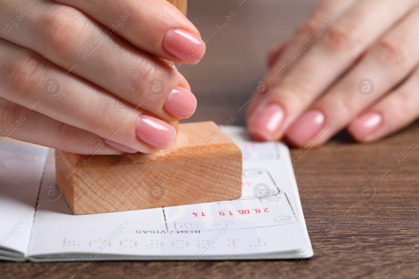 Photo of Ukraine, Lviv - September 6, 2022: Woman stamping visa page in passport at wooden table, closeup