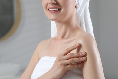 Woman applying body oil onto arm indoors, closeup