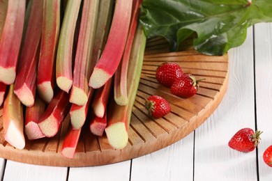 Photo of Cut fresh rhubarb stalks and strawberries on white wooden table, closeup