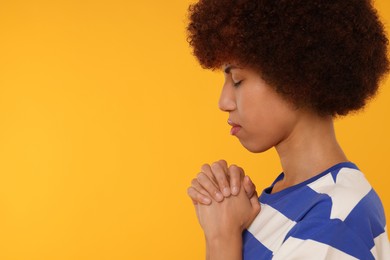 Photo of Woman with clasped hands praying to God on orange background. Space for text