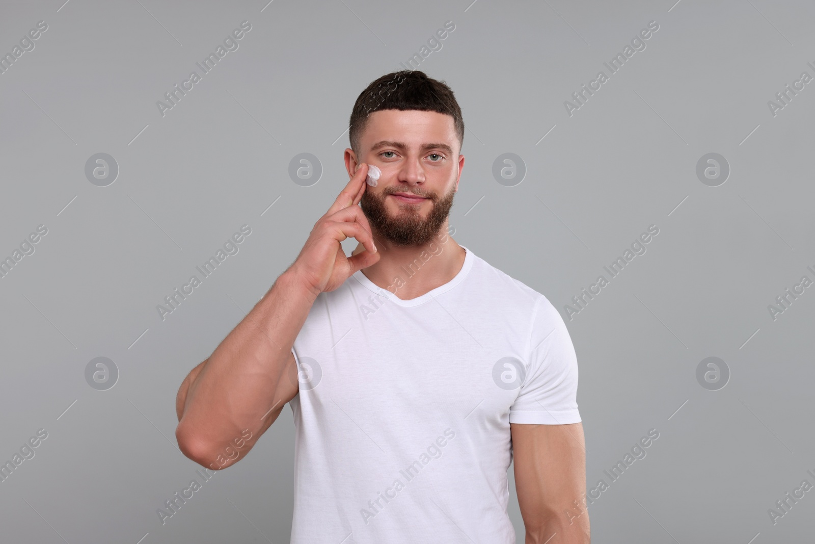 Photo of Handsome man applying cream onto his face on light grey background