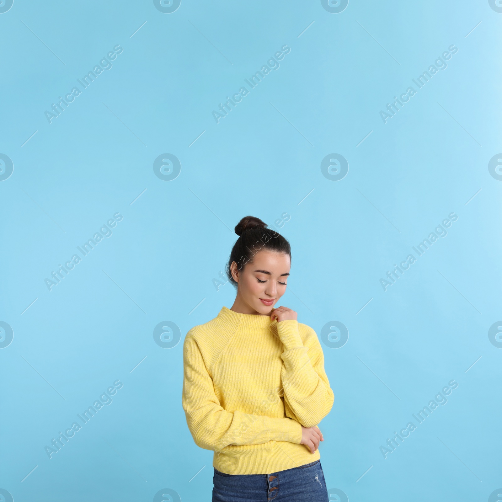 Photo of Beautiful young woman wearing yellow warm sweater on light blue background. Space for text